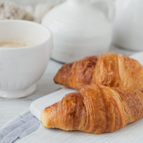 Delicious breakfast with fresh croissants and cup of coffee on white wooden background. Delicious Baking